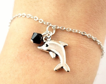 May include: A silver chain bracelet with a silver dolphin charm and a black crystal bead.
