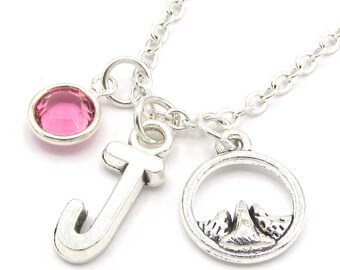 May include: A silver necklace with a pink crystal charm, a letter J charm, and a mountain charm.