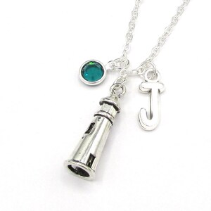 May include: Silver necklace with a lighthouse charm, a letter J charm, and a teal blue crystal.