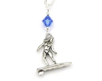 May include: A silver necklace with a blue crystal charm and a silver pendant of a woman surfing on a wave.