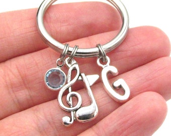 May include: Silver key chain with a treble clef charm, a letter G charm, and a light blue crystal charm.