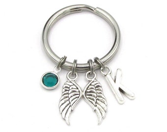 May include: Silver key chain with a teal blue crystal charm, two angel wing charms, and a letter K charm.
