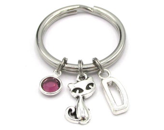 May include: Silver keyring with a pink rhinestone, a silver cat charm, and a silver charm with the letter D.