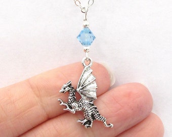 May include: A silver dragon pendant necklace with a light blue crystal charm. The dragon is in flight with its wings spread out.