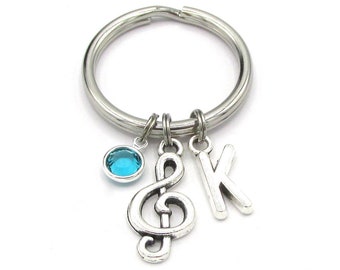 May include: A silver key chain with a treble clef charm, a letter K charm, and a light blue crystal charm.