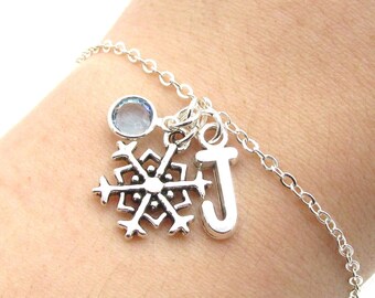May include: A silver chain bracelet with a snowflake charm, a light blue crystal charm, and a letter 'J' charm.