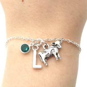 May include: A silver charm bracelet with a cow charm, a letter L charm, and a green crystal charm.