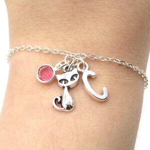 May include: A silver chain bracelet with a pink crystal charm, a silver cat charm, and a silver letter C charm.