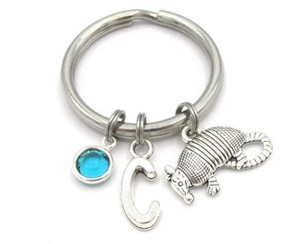 May include: A silver keyring with a blue crystal charm, a silver letter 'C' charm, and a silver armadillo charm.