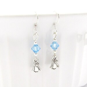 May include: Silver dangle earrings with a light blue crystal and a silver penguin charm.