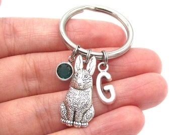 May include: Silver key chain with a rabbit charm, a green crystal charm, and a letter G charm.