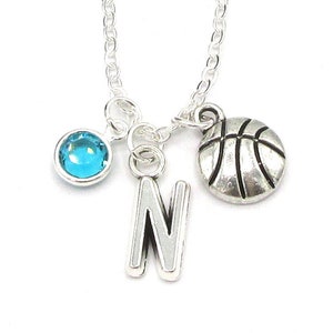 May include: Silver necklace with a basketball charm, a blue crystal charm, and a letter N charm.