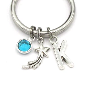 May include: A silver keychain with a blue crystal charm, a silver star charm, and a silver letter K charm.