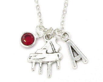 May include: Silver necklace with a red gemstone, a piano charm, and a letter 'A' charm.