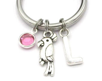 May include: A silver key chain with a pink rhinestone charm, a silver parrot charm, and a silver letter L charm.