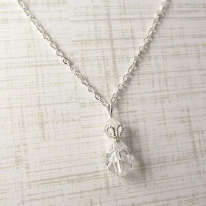 May include: A silver chain necklace with a clear crystal pendant. The pendant is shaped like a teardrop and has a silver filigree design.