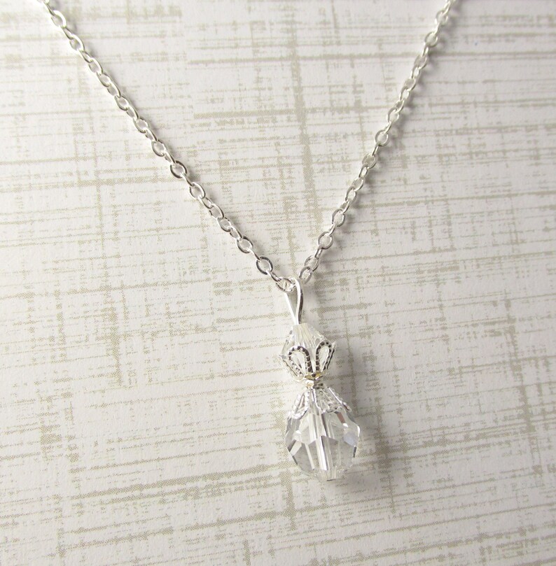 May include: A silver chain necklace with a clear crystal pendant. The pendant is shaped like a teardrop and has a silver filigree design.