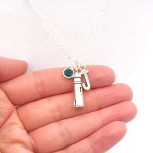 May include: Silver necklace featuring a lighthouse charm, a small green gemstone, and a letter 'J' charm.