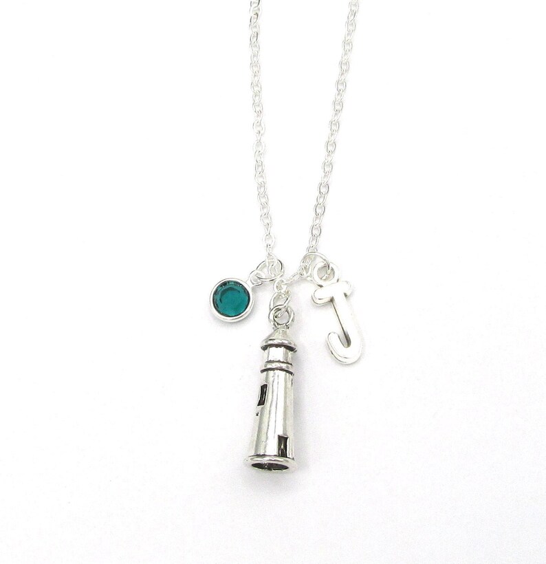 May include: Silver necklace with a lighthouse charm, a teal blue crystal charm, and a silver letter J charm.