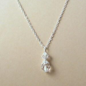 May include: A silver chain necklace with a clear crystal pendant. The pendant is faceted and has a silver filigree design.