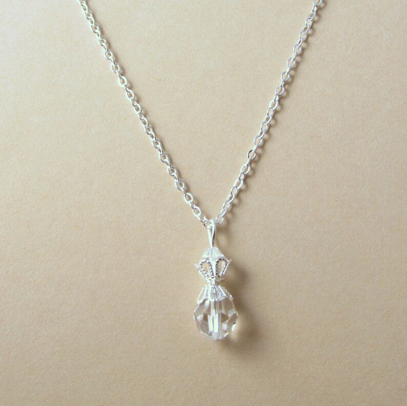 May include: A silver chain necklace with a clear crystal pendant. The pendant is faceted and has a silver filigree design.