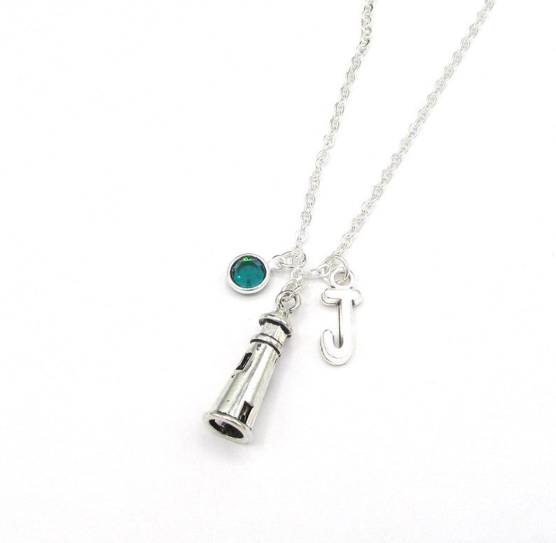 May include: Silver necklace with a lighthouse charm, a letter J charm, and a teal blue crystal.