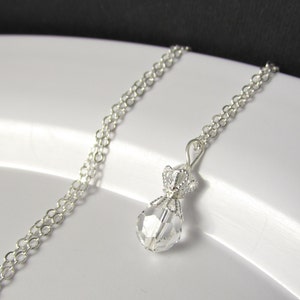 May include: A silver chain necklace with a clear crystal pendant shaped like a money bag. The pendant has a silver crown on top.
