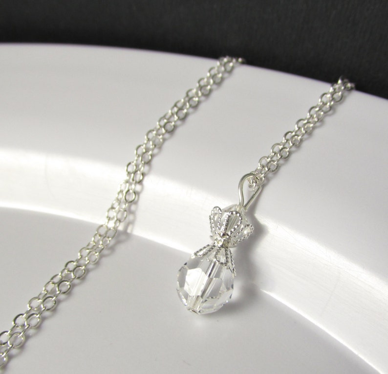 May include: A silver chain necklace with a clear crystal pendant shaped like a money bag. The pendant has a silver crown on top.