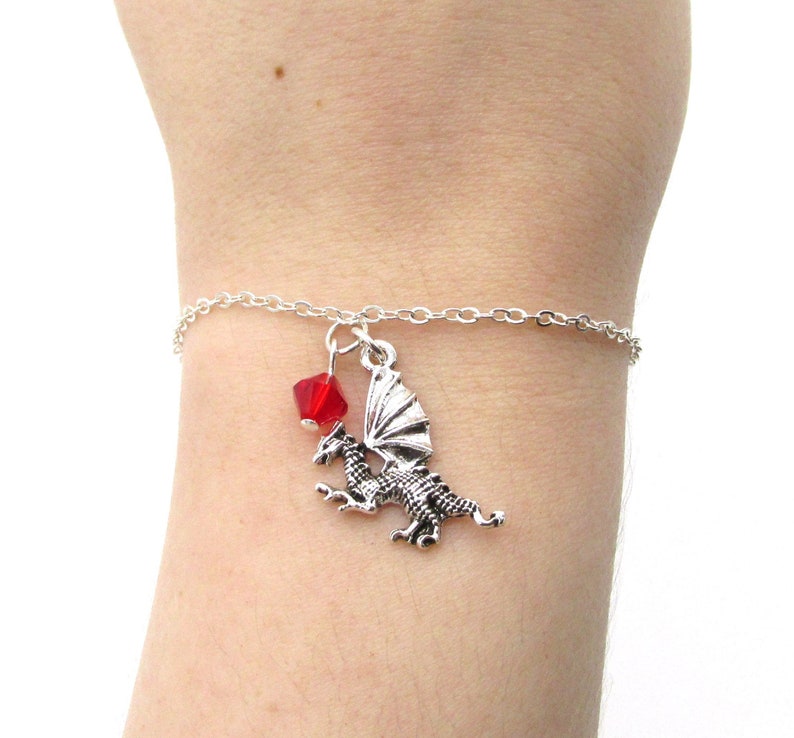 May include: A silver chain bracelet with a silver dragon charm and a red crystal bead.