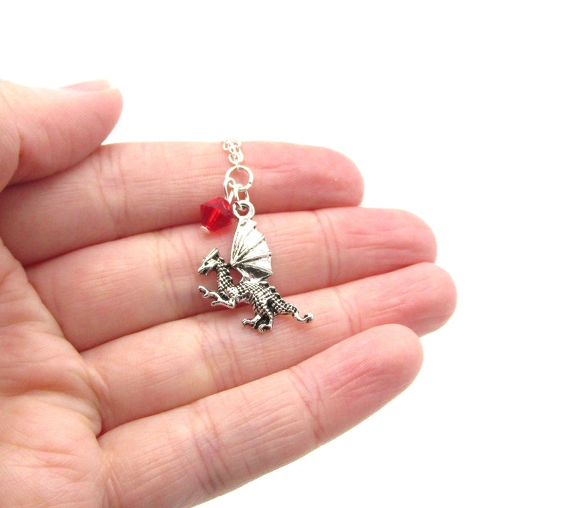 May include: Silver dragon pendant necklace with a red crystal charm. The dragon is in flight with its wings spread.