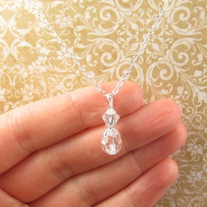 May include: A silver chain necklace with a clear crystal pendant shaped like a money bag.