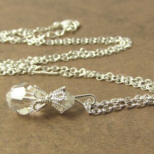 May include: A silver chain necklace with a clear crystal pendant. The pendant is shaped like a teardrop and has a delicate silver design.