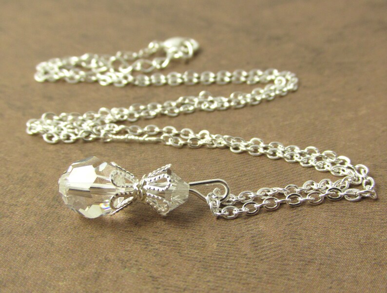 May include: A silver chain necklace with a clear crystal pendant. The pendant is shaped like a teardrop and has a delicate silver design.