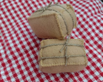 May include: Two beige felt bundles tied with twine, resting on a red and white checkered cloth. The bundles are rectangular with rounded edges and stitched seams. The twine is wrapped around the bundles.