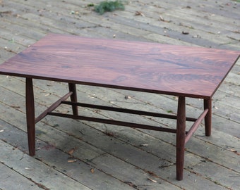 May include: A dark brown wooden coffee table with a rectangular top and a simple, mid-century modern design. The table has a lower shelf and four slender legs.