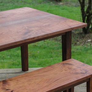 May include: A wooden table and bench set with a natural wood finish. The table has a rectangular top and four legs. The bench has a rectangular top and four legs. The table and bench are both made of solid wood.
