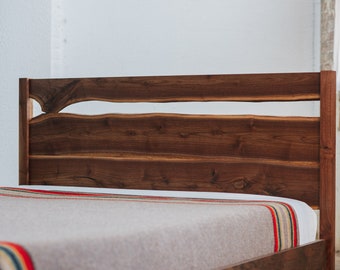 May include: A wooden bed frame with a headboard made of natural walnut wood with a unique cutout design. The headboard is made of several planks of wood that are joined together. The bed frame is a dark brown color.