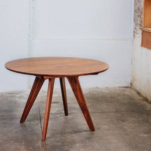 May include: A round wooden table with a brown top and three legs. The table is made of solid wood and has a natural finish.