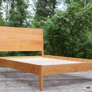 May include: A wooden bed frame with a slatted headboard and footboard. The frame is made of natural wood and has a simple, modern design.