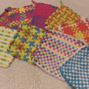 May include: A set of eight colorful woven pot holders in various patterns, including stripes, checks, and diamonds. The pot holders are made with a white base and feature bright colors like yellow, green, blue, pink, and orange.