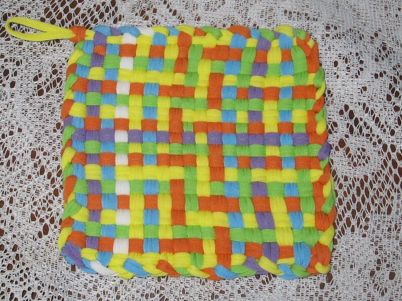 May include: A colorful woven pot holder with a yellow, orange, green, blue, and purple pattern. The pot holder has a loop for hanging.