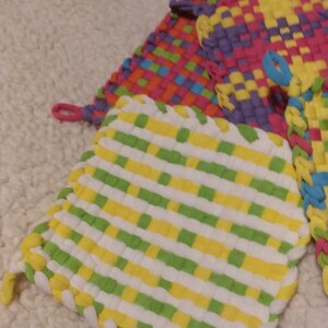 May include: Three woven pot holders in a variety of colors, including green, yellow, white, purple, pink, orange, and blue. The pot holders are made of a soft, textured fabric and have a woven design.