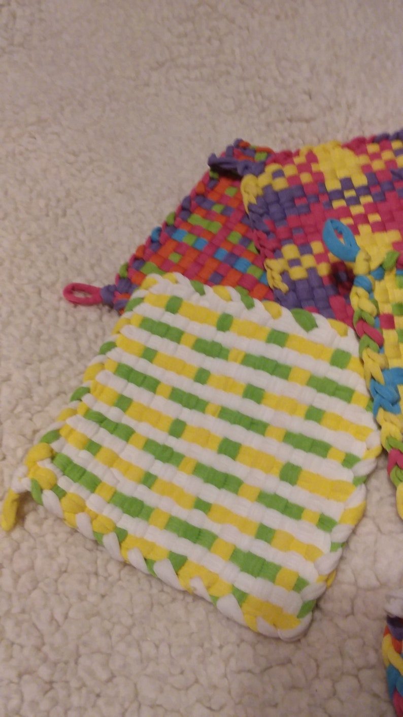 May include: Three woven pot holders in a variety of colors, including green, yellow, white, purple, pink, orange, and blue. The pot holders are made of a soft, textured fabric and have a woven design.