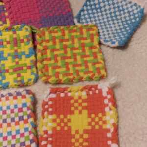 May include: A set of six colorful woven pot holders with different patterns. The pot holders are made with a variety of colors, including pink, purple, yellow, green, blue, orange, and white.
