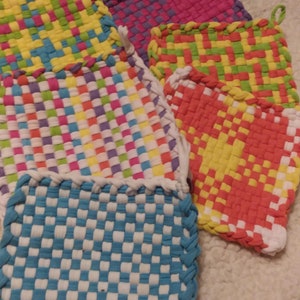 May include: A set of colorful woven pot holders, featuring a variety of patterns and colors, including blue, white, yellow, green, pink, and orange. The pot holders are made from woven fabric and have a braided edge.