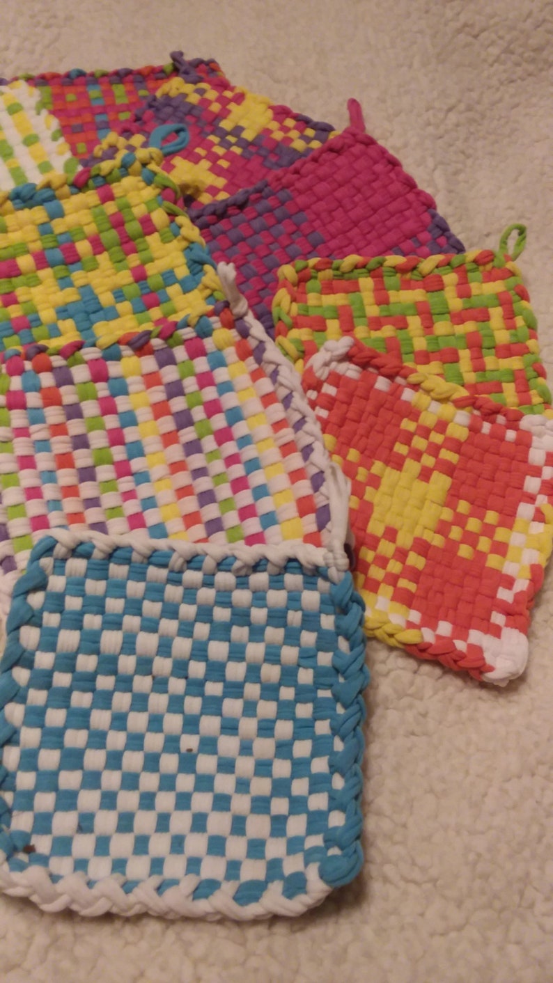 May include: A set of colorful woven pot holders, featuring a variety of patterns and colors, including blue, white, yellow, green, pink, and orange. The pot holders are made from woven fabric and have a braided edge.