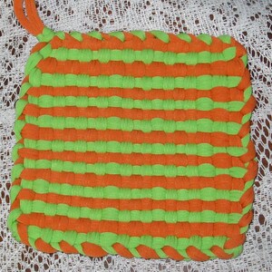 May include: A green and orange woven pot holder made from strips of fabric.