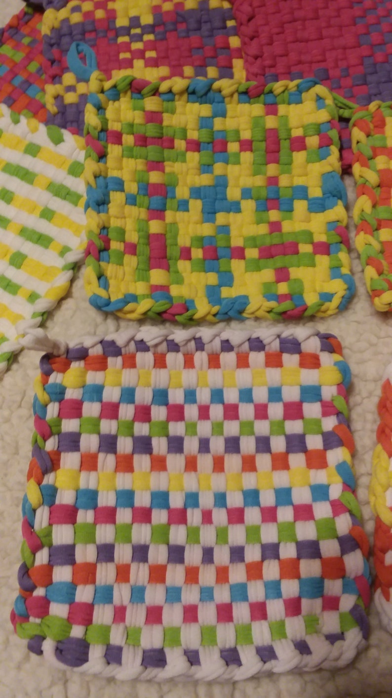 May include: Four colorful woven pot holders with a checkered pattern. The pot holders are made of fabric strips in shades of purple, green, yellow, orange, pink, blue, and white.