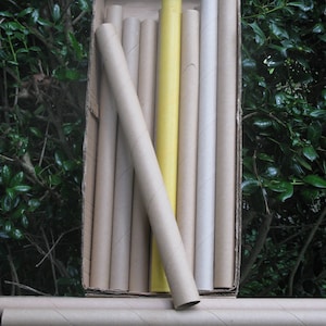 May include: A collection of cardboard tubes, some arranged inside a cardboard box. The tubes are primarily tan, with one yellow tube standing out. The tubes are of varying lengths and diameters, suitable for crafts or packaging.