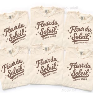 May include: Six cream-colored t-shirts with the text "Fleur du Soleil" in brown script and the words "Mockup Studio" below. The shirts are laid flat, showcasing the design on the front. The design includes star accents.